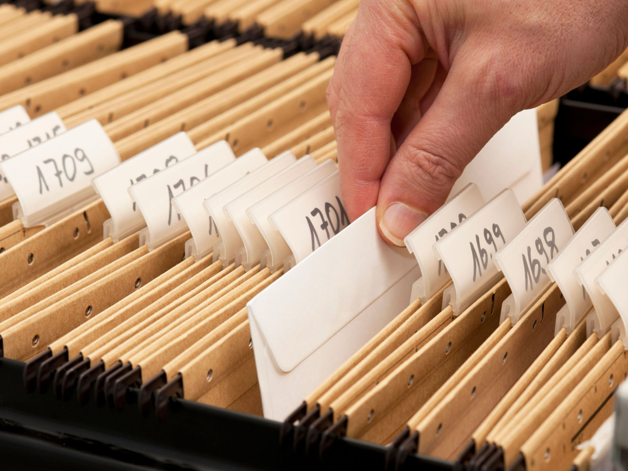 A hand pulling a labeled file from an organized row of hanging folders