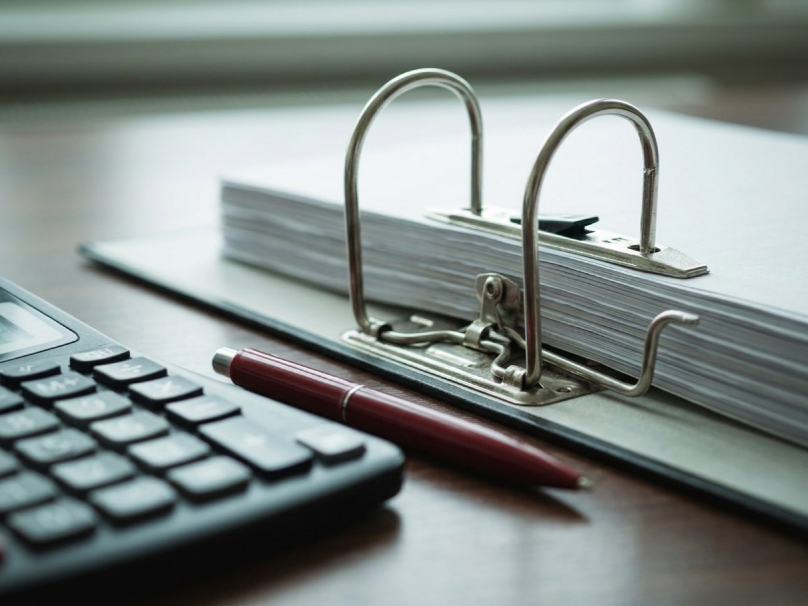 Lever-arch binder full of paper with its rings open beside a calculator and a red pen