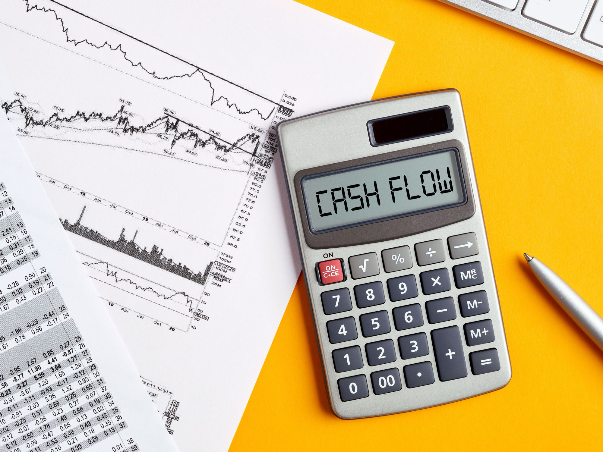Calculator displaying CASH FLOW beside financial charts and a printed spreadsheet