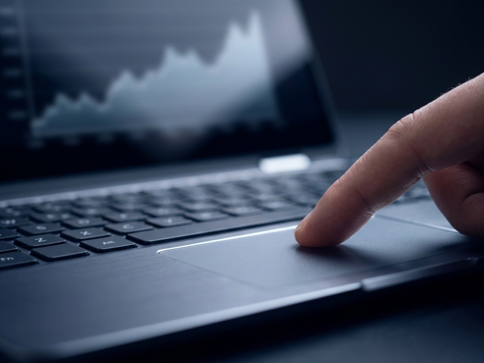 Finger pressing the trackpad of a laptop with a line graph rising on the screen