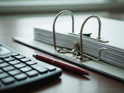 Lever-arch binder full of paper with its rings open beside a calculator and a red pen