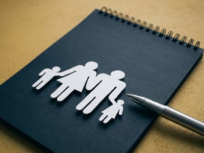Paper cutout of a family of four on a dark spiral notebook beside a pen