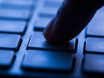 Fingertip pressing a key on a computer keyboard in dim blue light