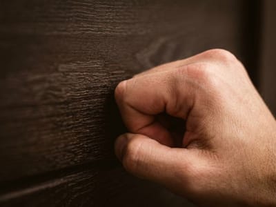 Fist knocking on a dark wooden door in close-up